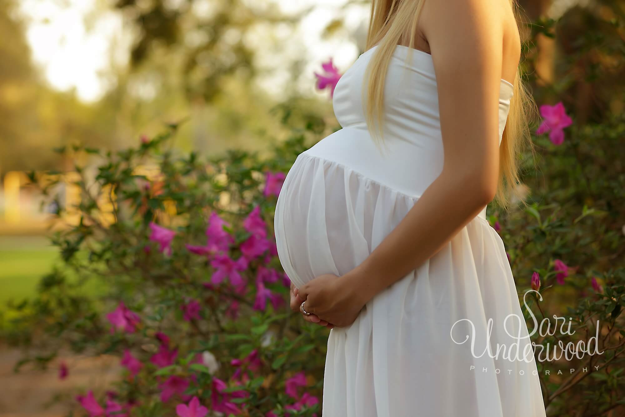 expectant mom in white dress near flowers