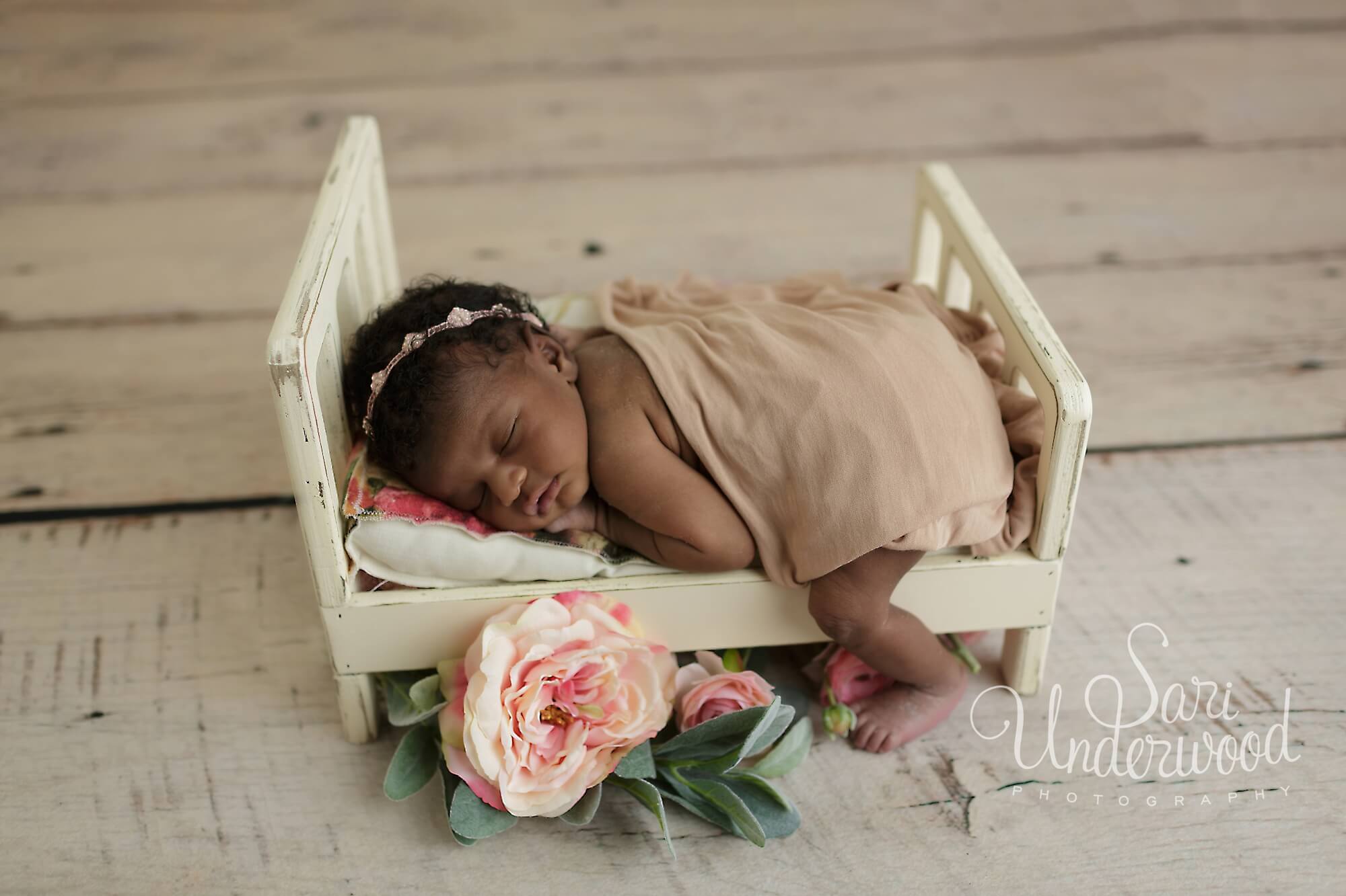 newborn baby girl posed on a tiny wooden bed