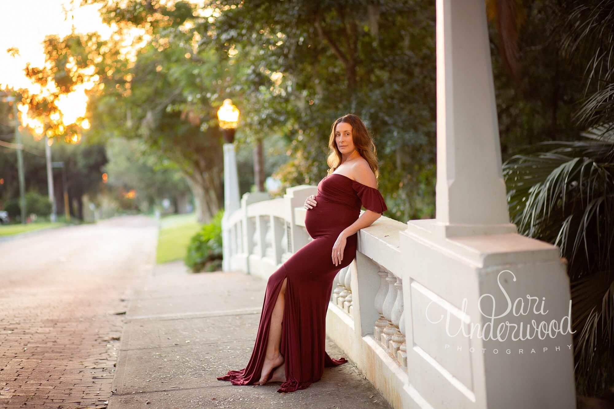 pregnant woman in a wine-colored gown leaning against a white bridge