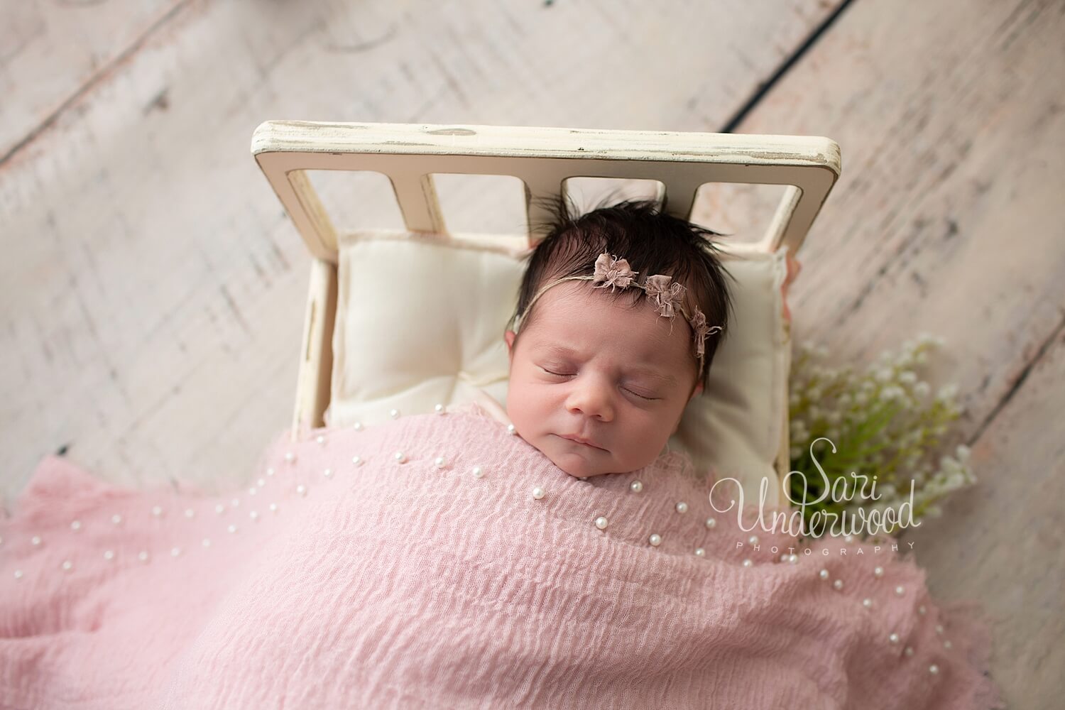 new baby girl in a tiny bed with pale pink blanket