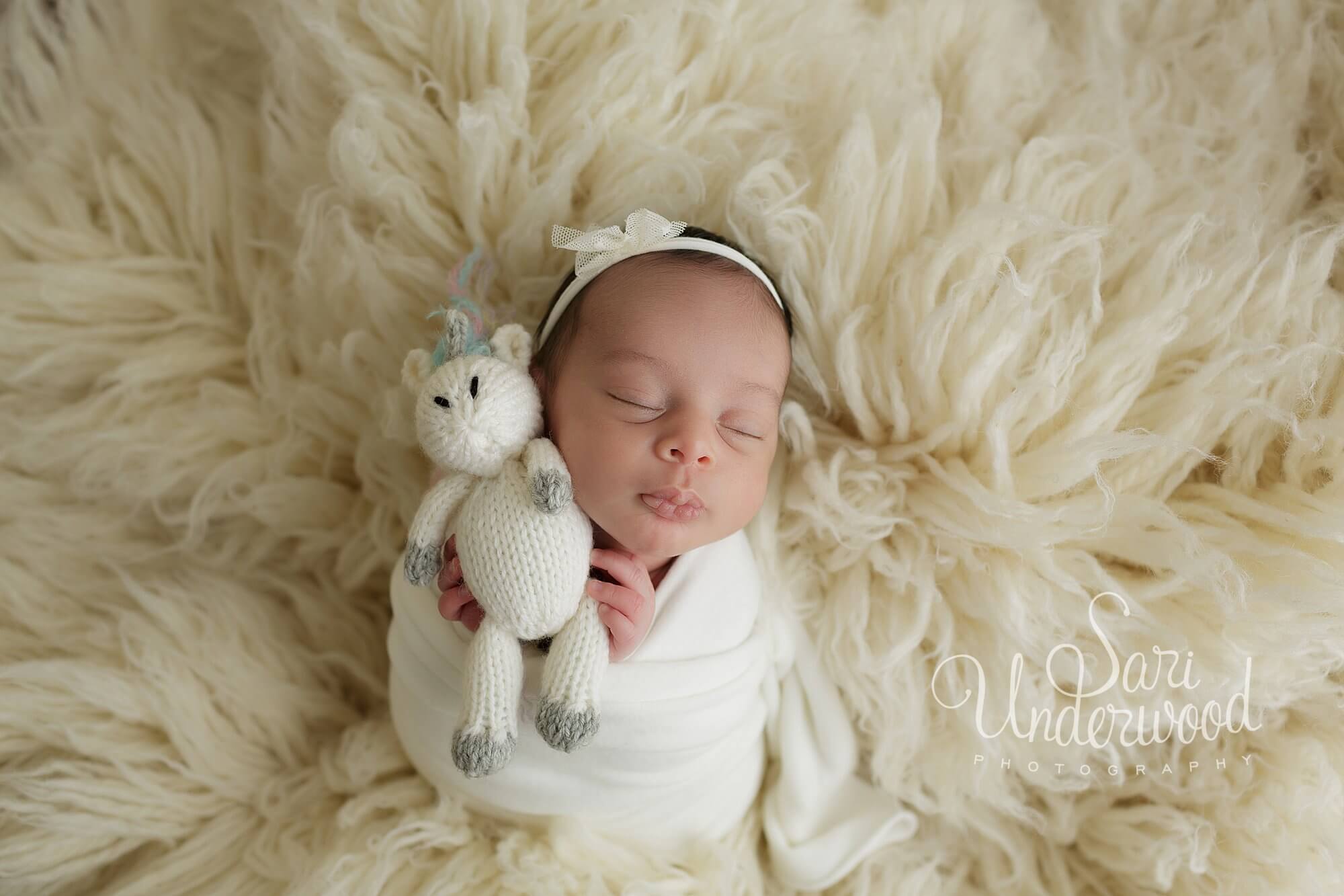newborn baby girl in swaddle holding unicorn stuffed animal